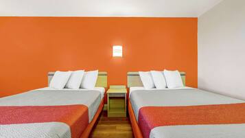 Una camera d'albergo con due letti, pareti arancioni, un comodino e un tavolino.