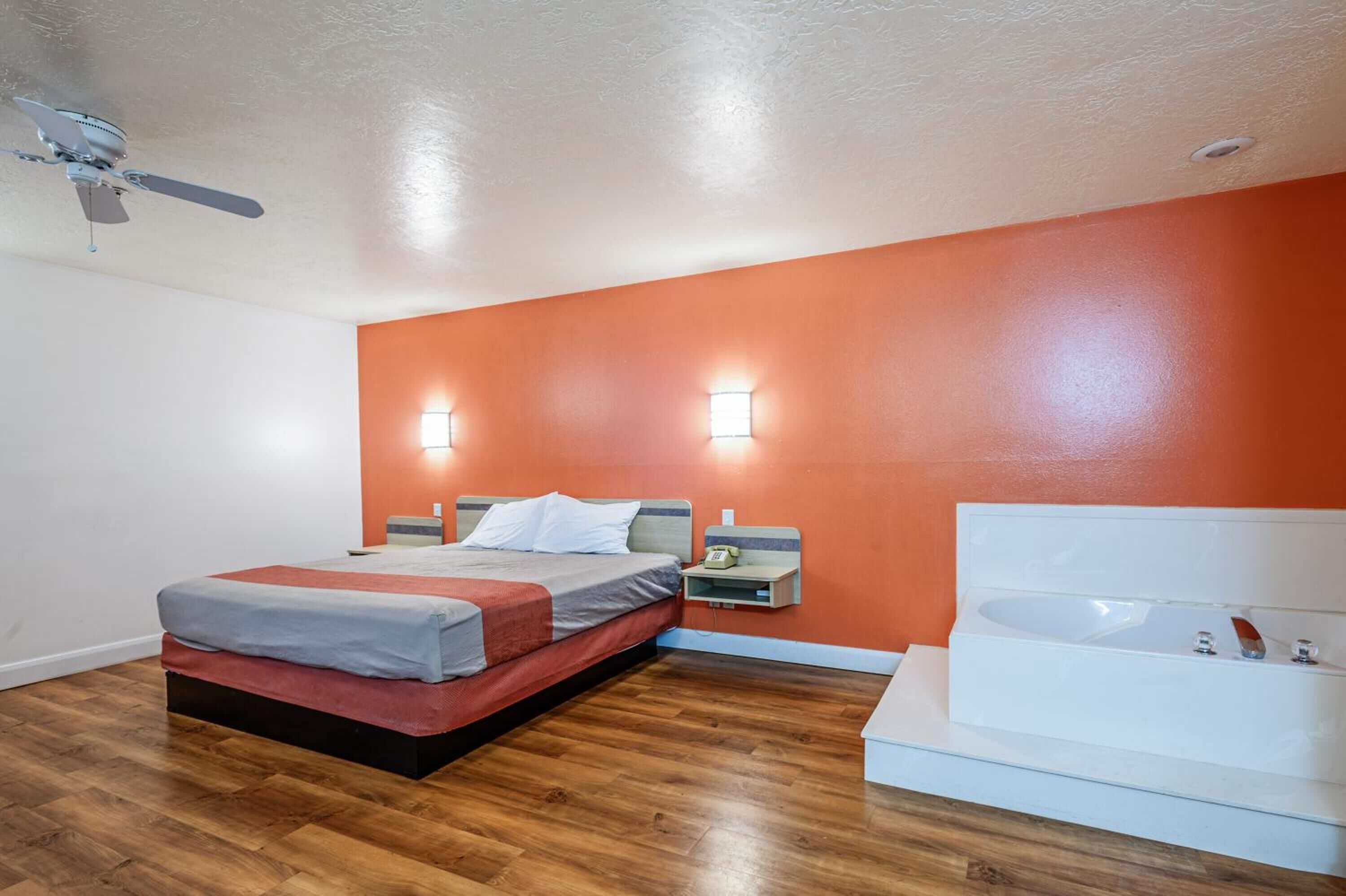 A bedroom with a bed, bedside table, nightstand, and a large bathtub.