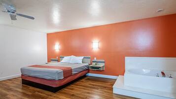 A bedroom with a bed, bedside table, nightstand, and a large bathtub.