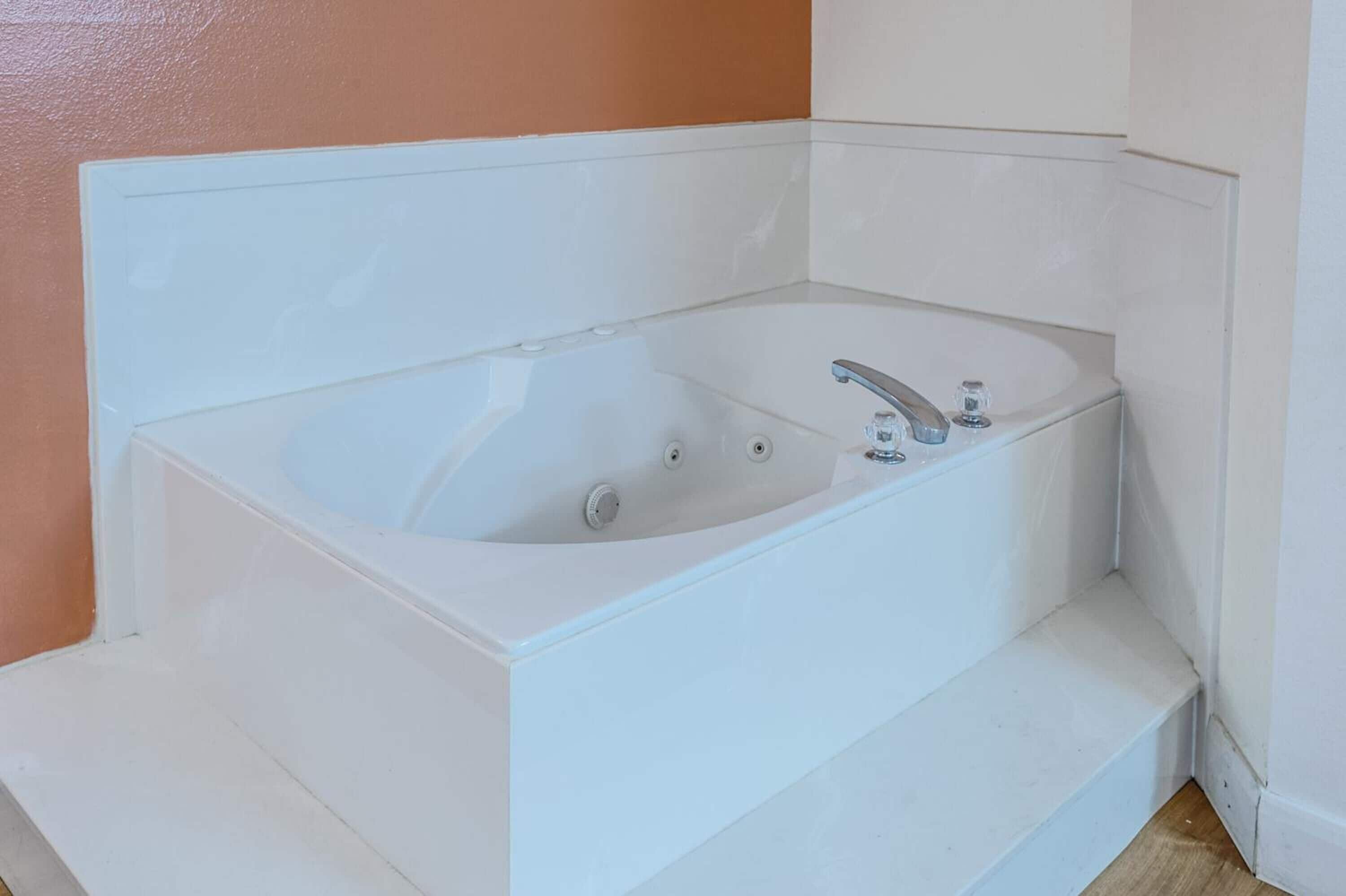 A white bathtub with two faucets and a control knob, set against a peach wall.