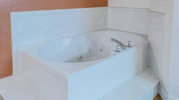 A white bathtub with two faucets and a control knob, set against a peach wall.