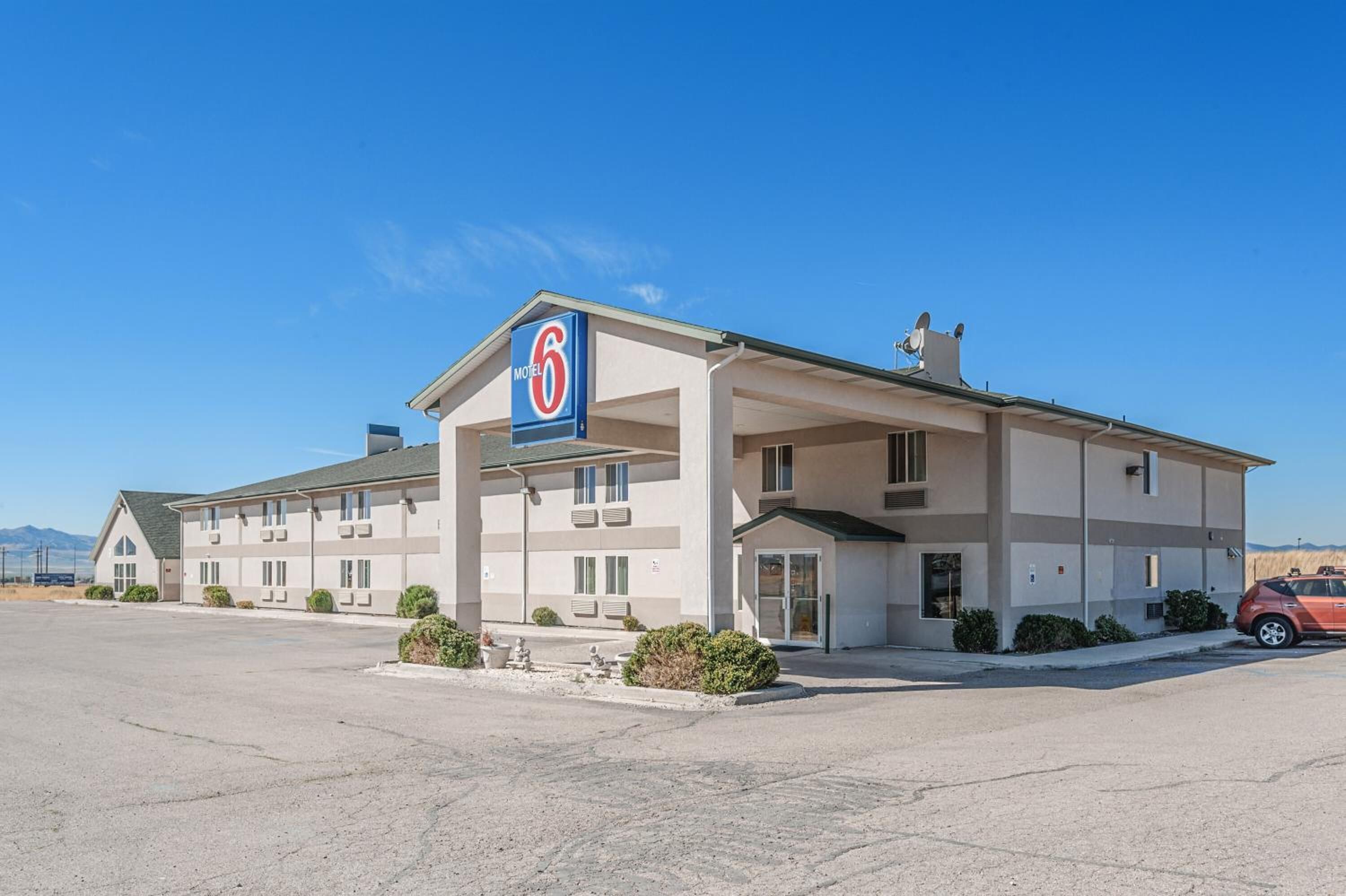 A motel with a prominent '6' sign, a covered parking area, and a clear sky.