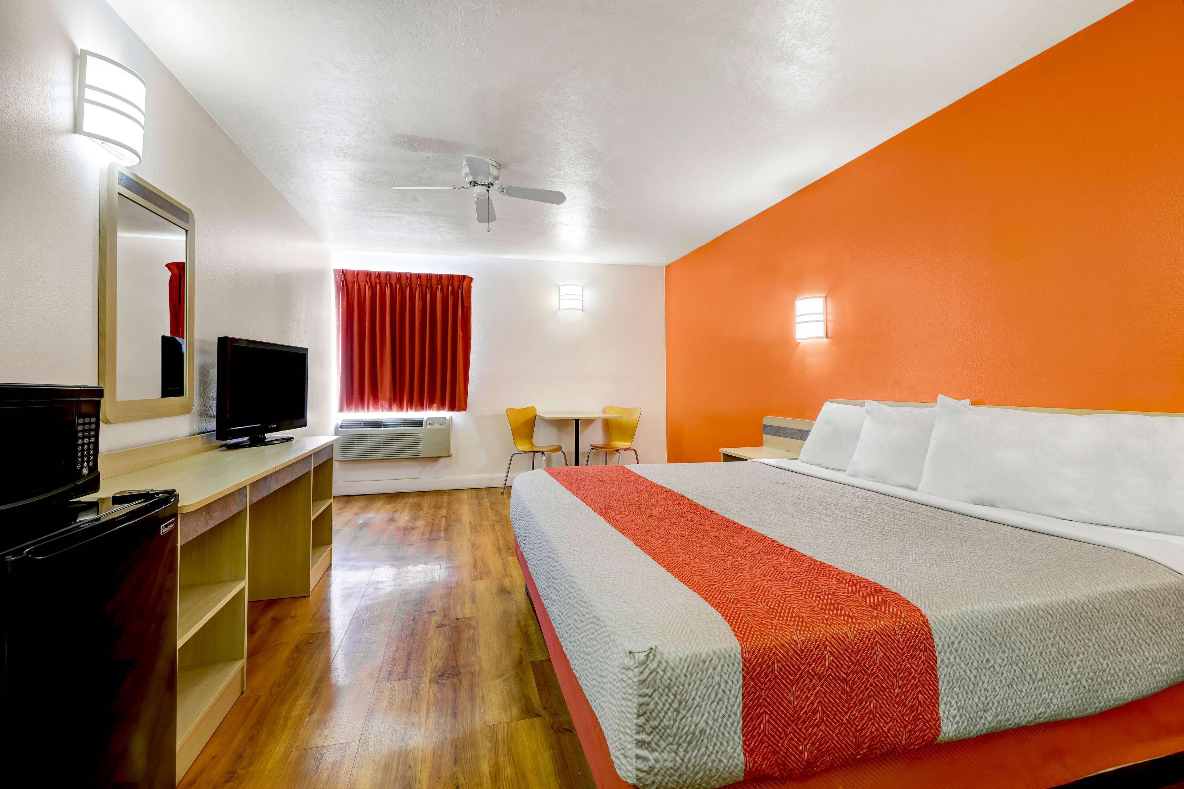 A hotel room with a bed, a desk, a television, and a ceiling fan.