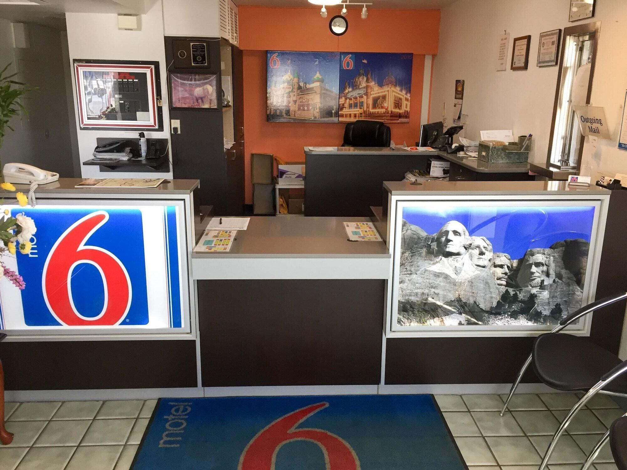 Un mostrador de recepción con un letrero grande con el número '6', un reloj y un letrero en el suelo que dice 'motel'.