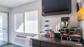 Habitación de hotel con kitchenette, televisor montado en la pared y ventana con persianas.