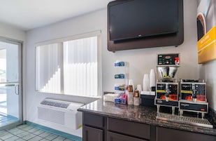 Habitación de hotel con kitchenette, televisor montado en la pared y ventana con persianas.