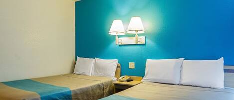 Habitación de hotel con dos camas, cada una con colcha azul y color beige, almohadas blancas y una mesita de noche con lámpara y teléfono.