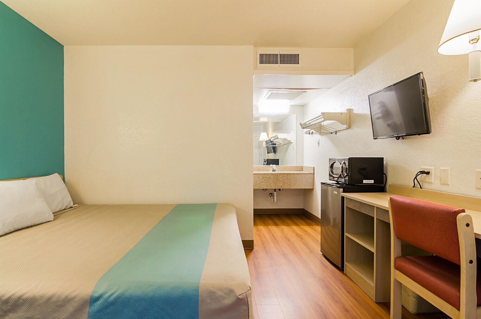 A hotel room with a bed, a desk with a chair, a television, and a kitchenette.