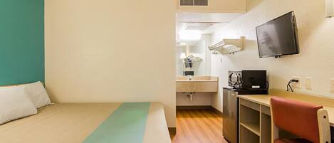 A hotel room with a bed, a desk with a chair, a television, and a kitchenette.
