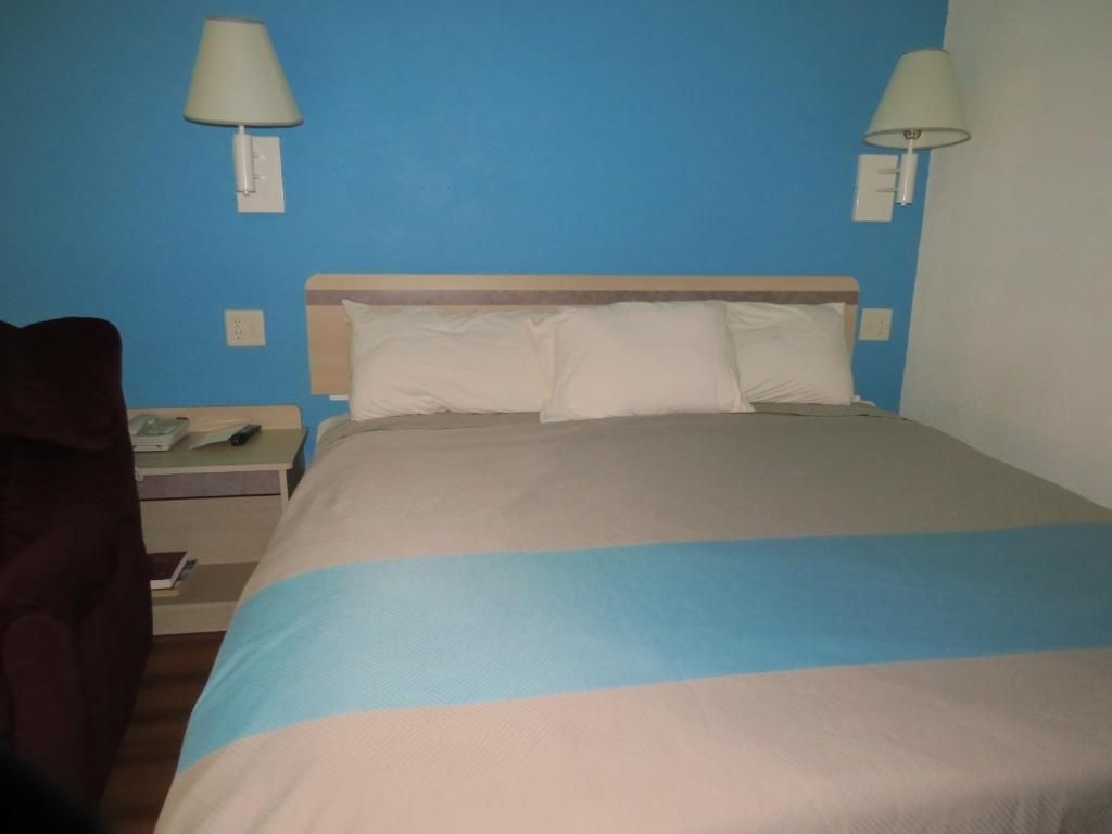A hotel room with a bed, two wall-mounted lamps, a nightstand with a phone, and a dark-colored armchair.