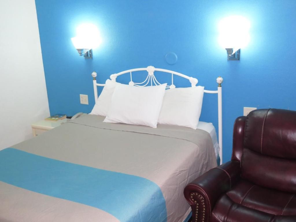 Ein Bett mit weißem Kopfteil, einer blauen Wand und einem roten Ledersessel.