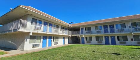 Ein zweistöckiges Motel mit Flachdach, mehreren Balkonen und einem begrünten Innenhof.