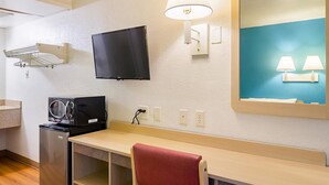 Ein Hotelzimmer mit Flachbildfernseher, Schreibtisch mit rotem Handtuch, integrierter Waschtrockner, Spiegel mit blauer Umrandung und Wandlampe.