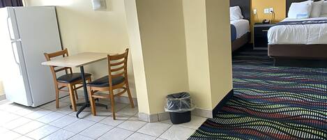 Una habitación de hotel con cama, escritorio con silla, un cesto de basura y una alfombra estampada.