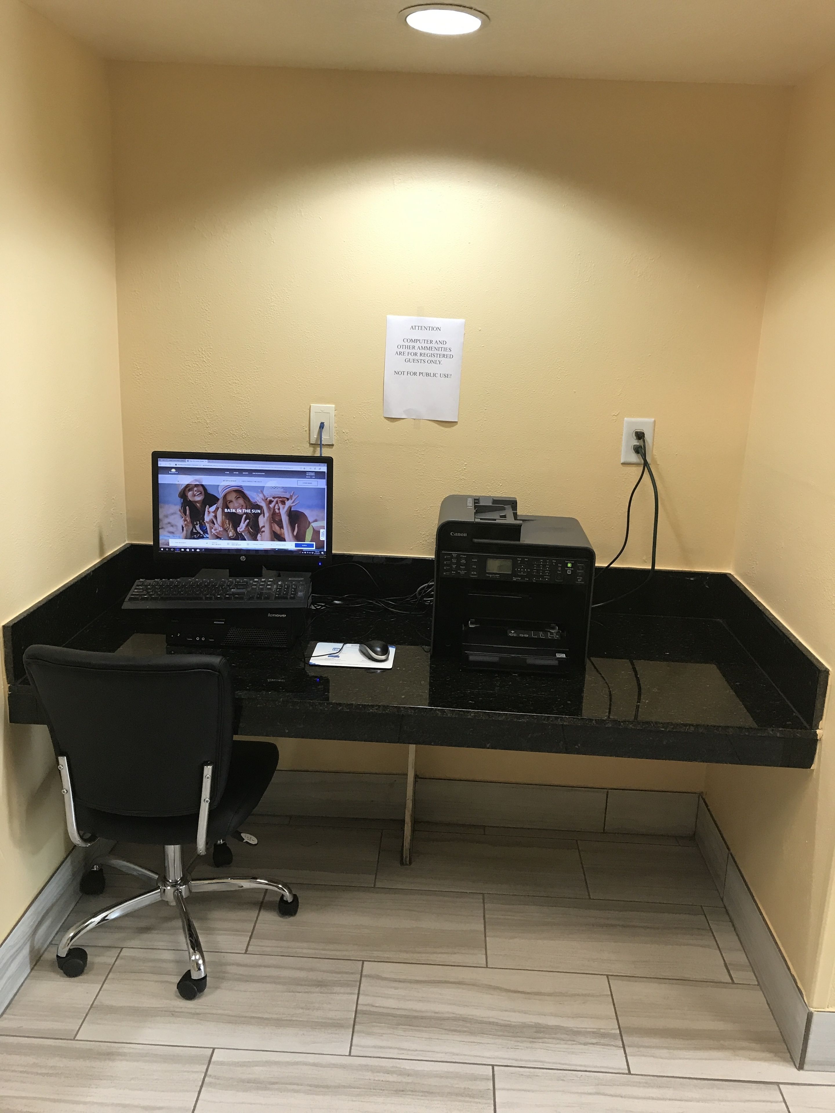 A computer desk with a laptop, printer, and keyboard. There is a chair in front of the desk.