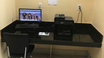 A computer desk with a laptop, printer, and keyboard. There is a chair in front of the desk.