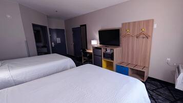 A hotel room with two beds, a TV, a desk with a computer, a microwave, and a wardrobe with hangers.