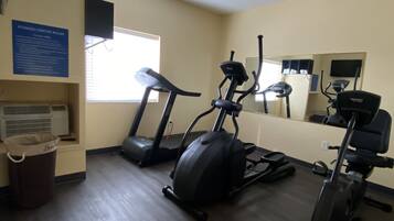 Centro de fitness com esteiras, elíptica e bicicleta ergométrica. Há um cesto de lixo e uma placa com regras.
