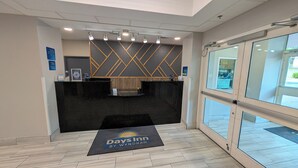 A reception area with a reception desk, a check-in counter, a digital display, and a glass door leading outside. - Days Inn & Suites by Wyndham Augusta Near Fort Eisenhower (Grovetown)