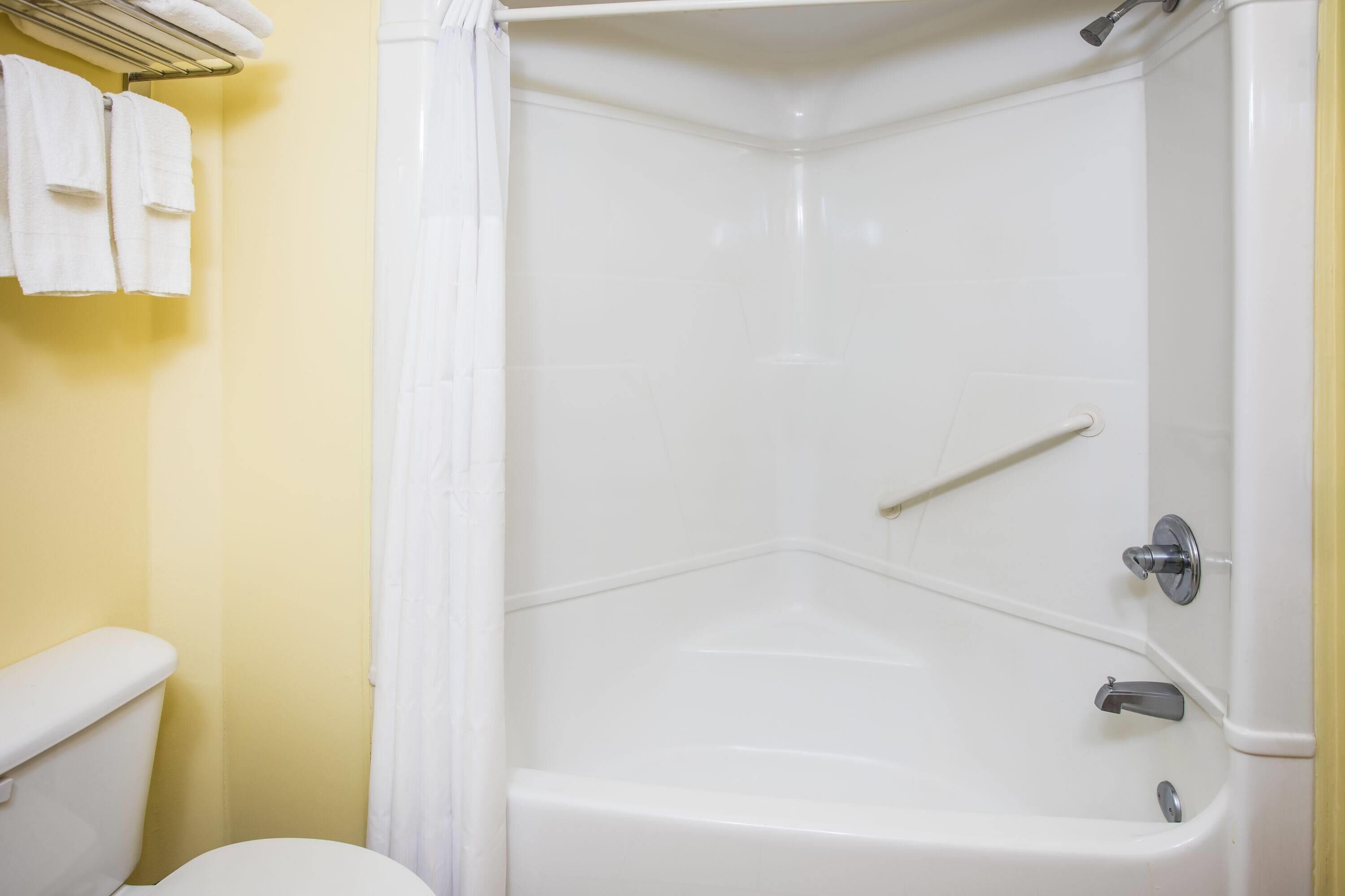 A corner shower with a white tub, a towel rack with towels, and a toilet.