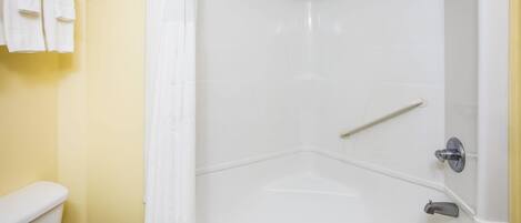 Um chuveiro no canto, uma banheira branca, um porta-toalhas com toalhas e um vaso sanitário.
