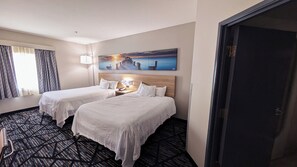 Une chambre d’hôtel avec deux lits, un tableau représentant un coucher de soleil, une lampe et une moquette à motifs.