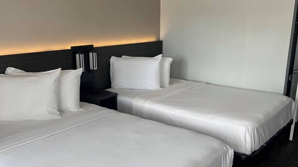 Une chambre d’hôtel avec deux lits, une tête de lit sombre et une table de chevet avec une lampe.