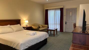 A hotel room with a bed, a chair, a table, a TV, and a window with curtains.