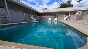 Una piscina con sillas blancas, un área cercada y un edificio con múltiples ventanas.