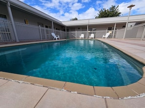 A swimming pool with white chairs, a fenced area, and a building with multiple windows.