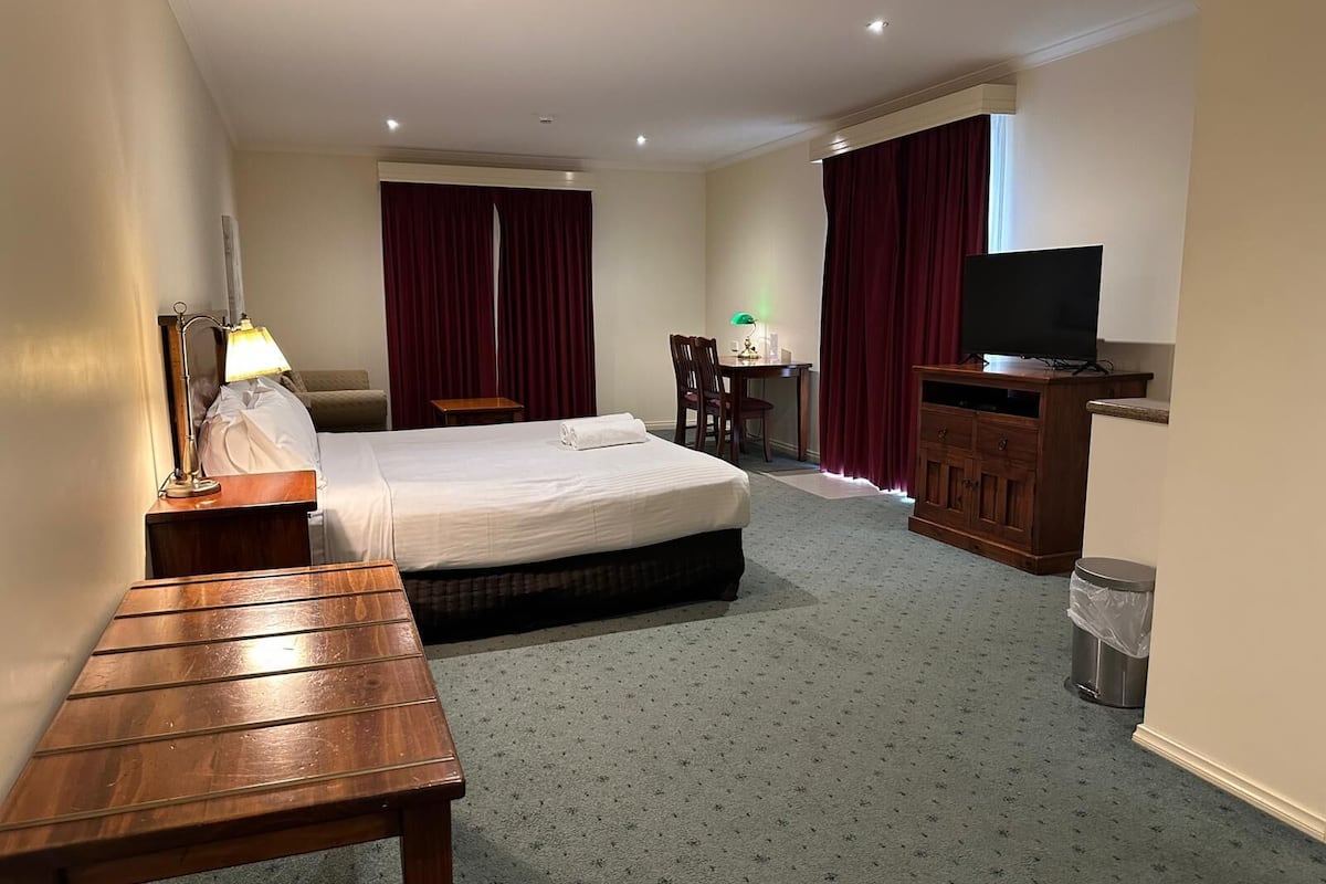 Ein Hotelzimmer mit Bett, Schreibtisch, Fernseher, Lampe und Stuhl.