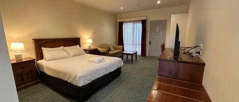 A hotel room with a bed, bedside tables, a desk, a chair, and a television.