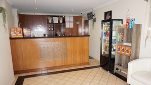 Un área de recepción con mostrador de madera, un refrigerador lleno de bebidas y una sala de estar con un sofá blanco.
