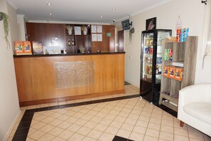 A reception area with a wooden counter, a refrigerator stocked with beverages, and a seating area with a white couch. - Crystal INN (Bendigo)