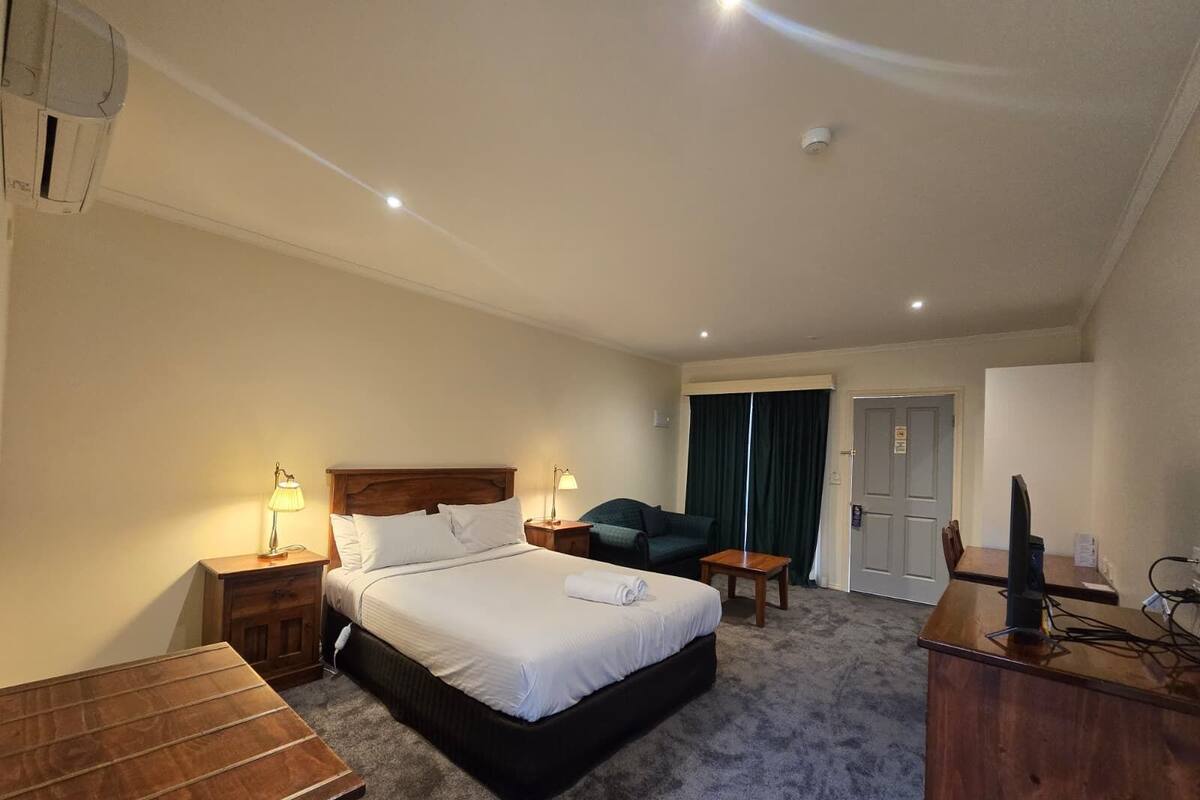 Ein Hotelzimmer mit Bett, Nachttischen, Schreibtisch, Stuhl, Fernseher und einer Tür.