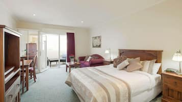 A hotel room with a large bed, a wooden dresser, a desk with a chair, a sofa, and a large window with curtains.