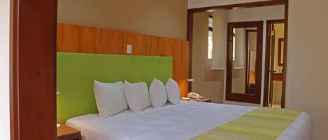 A hotel room with a bed, a bedside table, a mirror, and an air conditioning unit.