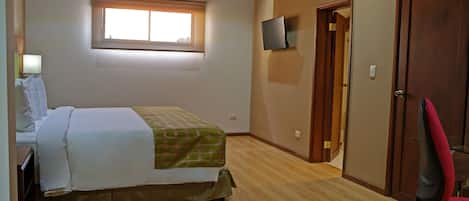 A bedroom with a bed, a television, a door, and a window.
