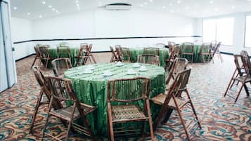 A conference room with round tables covered in green tablecloths, surrounded by wicker chairs.