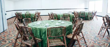 Un salón de conferencias con mesas redondas cubiertas con manteles verdes, rodeado de sillas de mimbre.