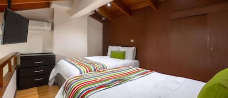 A bedroom with two beds, wooden ceiling beams, a flat-screen TV, and a wardrobe.