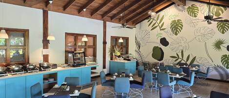 A restaurant with blue chairs, a counter with food display, and a wall with leaf patterns.