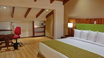 Habitación de hotel con cama, escritorio, silla, mesita de noche y cabecera verde.