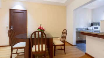 Un comedor con una mesa de vidrio y sillas de madera, una cocina con microondas y tostadora, y una puerta al fondo.