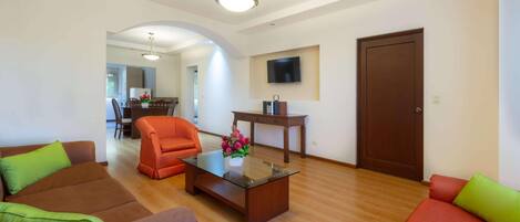 A living room with a glass coffee table, two sofas, a TV, and a wooden door.