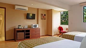 Une chambre d’hôtel avec deux lits, une télévision, un four à micro-ondes, un petit meuble et une fenêtre donnant sur un espace verdoyant.