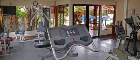 Une salle de sport équipée de machines de cardio, de poids et offrant une vue sur la piscine.