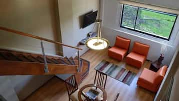 Una sala moderna con una escalera, sofás anaranjados, una mesa redonda y un amplio ventanal con vistas a zonas verdes.