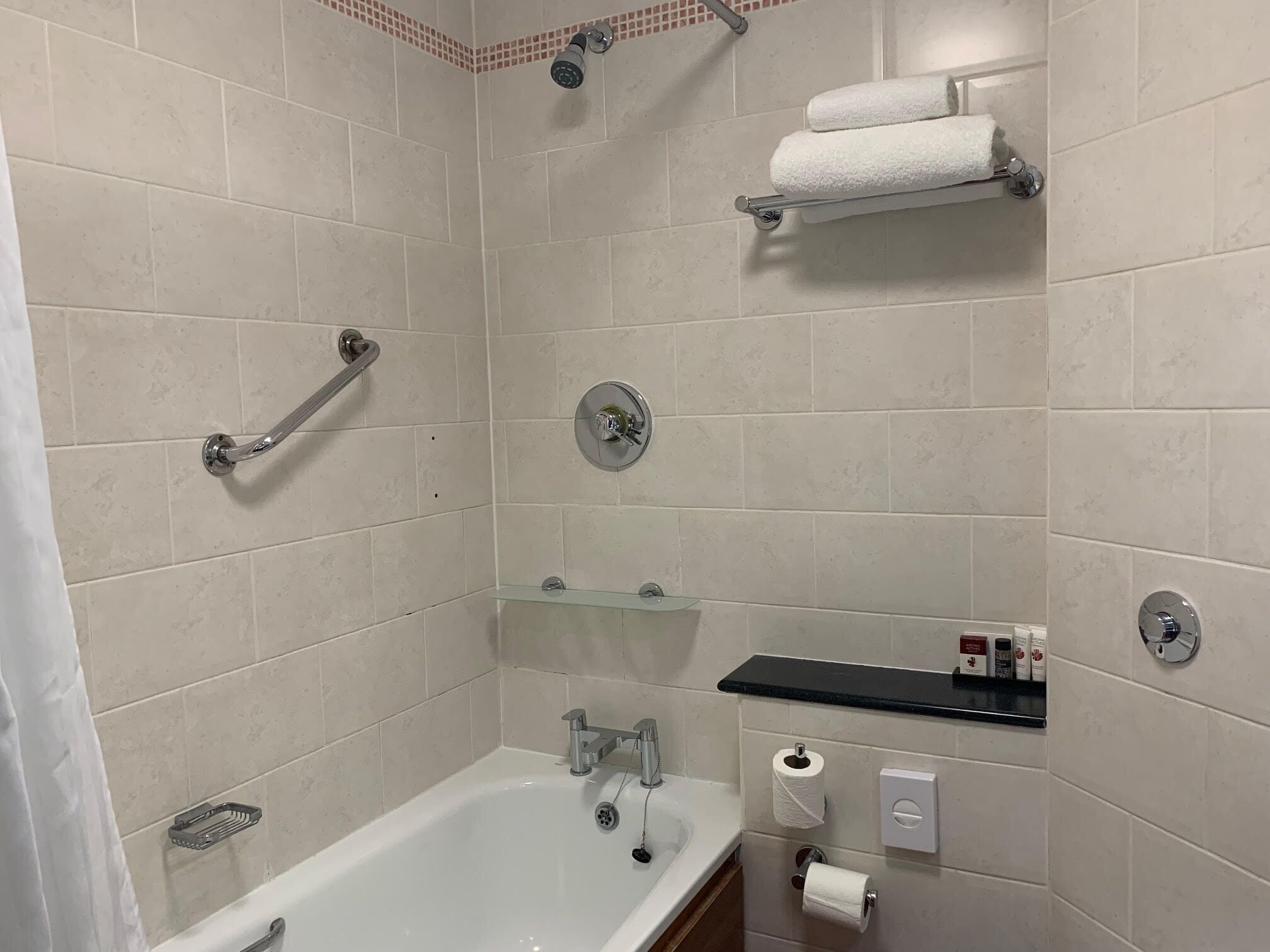 A modern bathroom with a bathtub, a shower with a handheld showerhead, a glass shelf, and a towel rack.