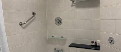A modern bathroom with a bathtub, a shower with a handheld showerhead, a glass shelf, and a towel rack.